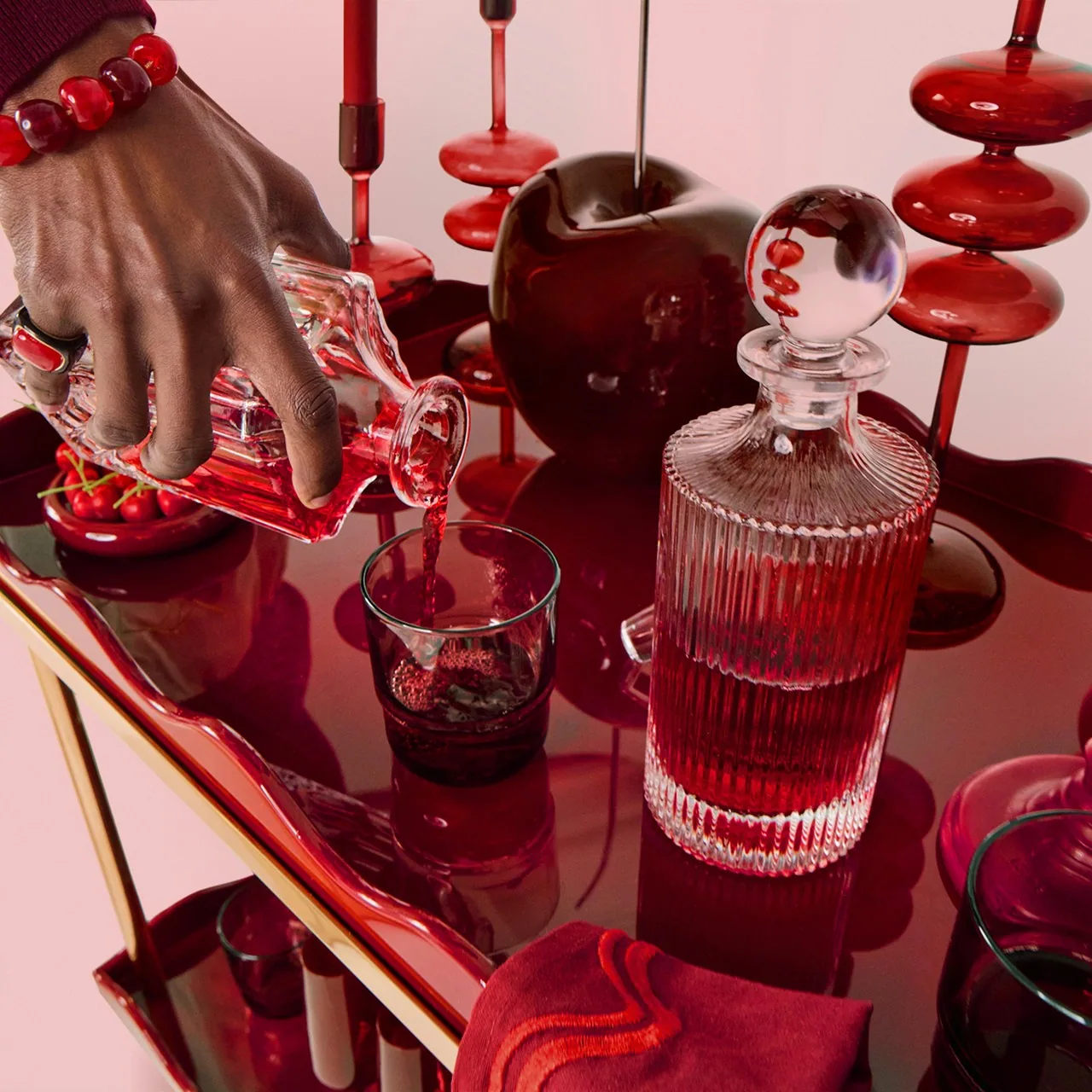 A hand lifting a red glass decanter from a styled tabletop