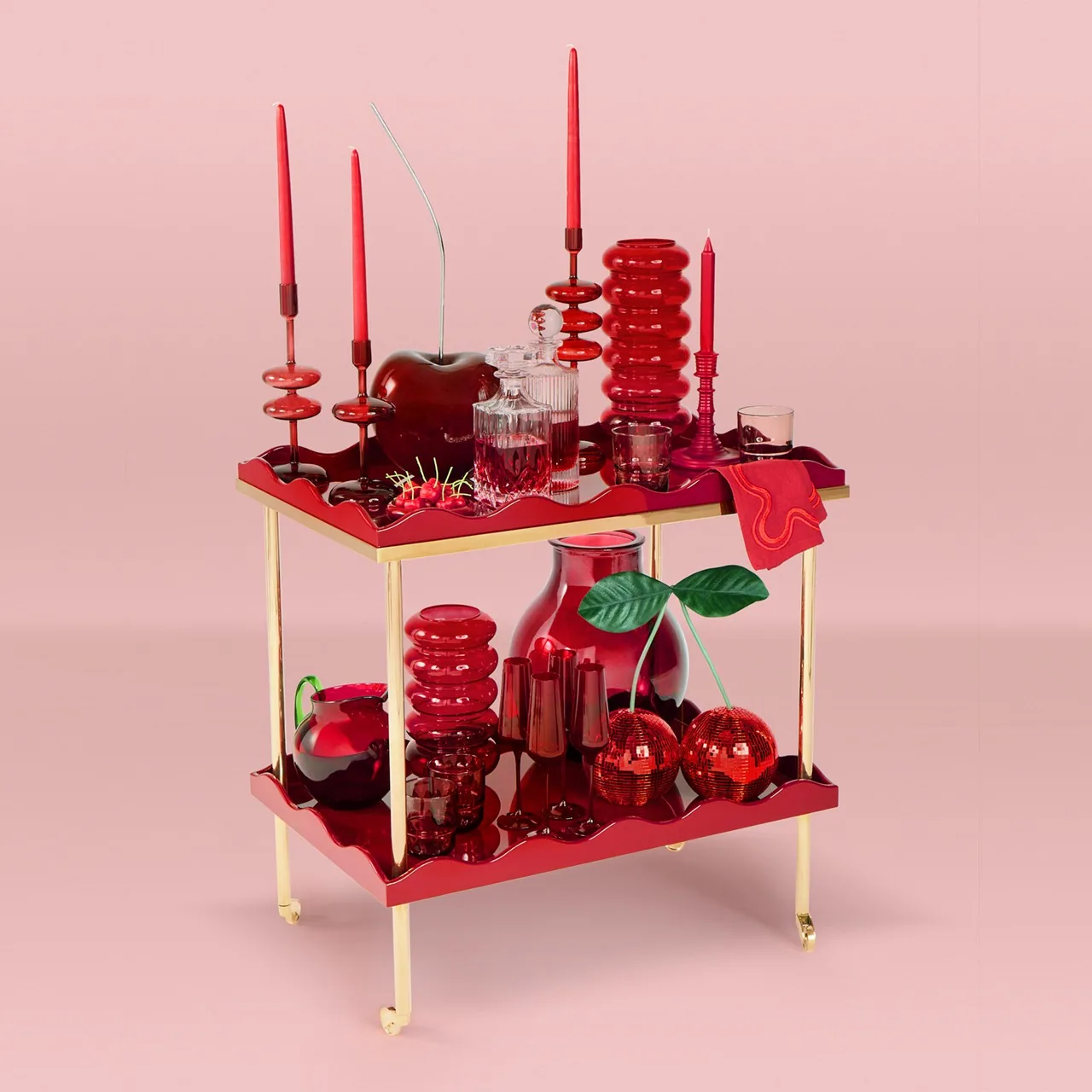 A gold bar cart styled with red glassware, candles and cherries