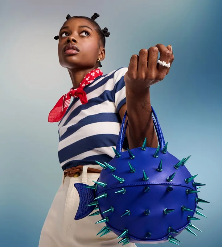 A model holding a blue spiked handbag shaped like a pufferfish