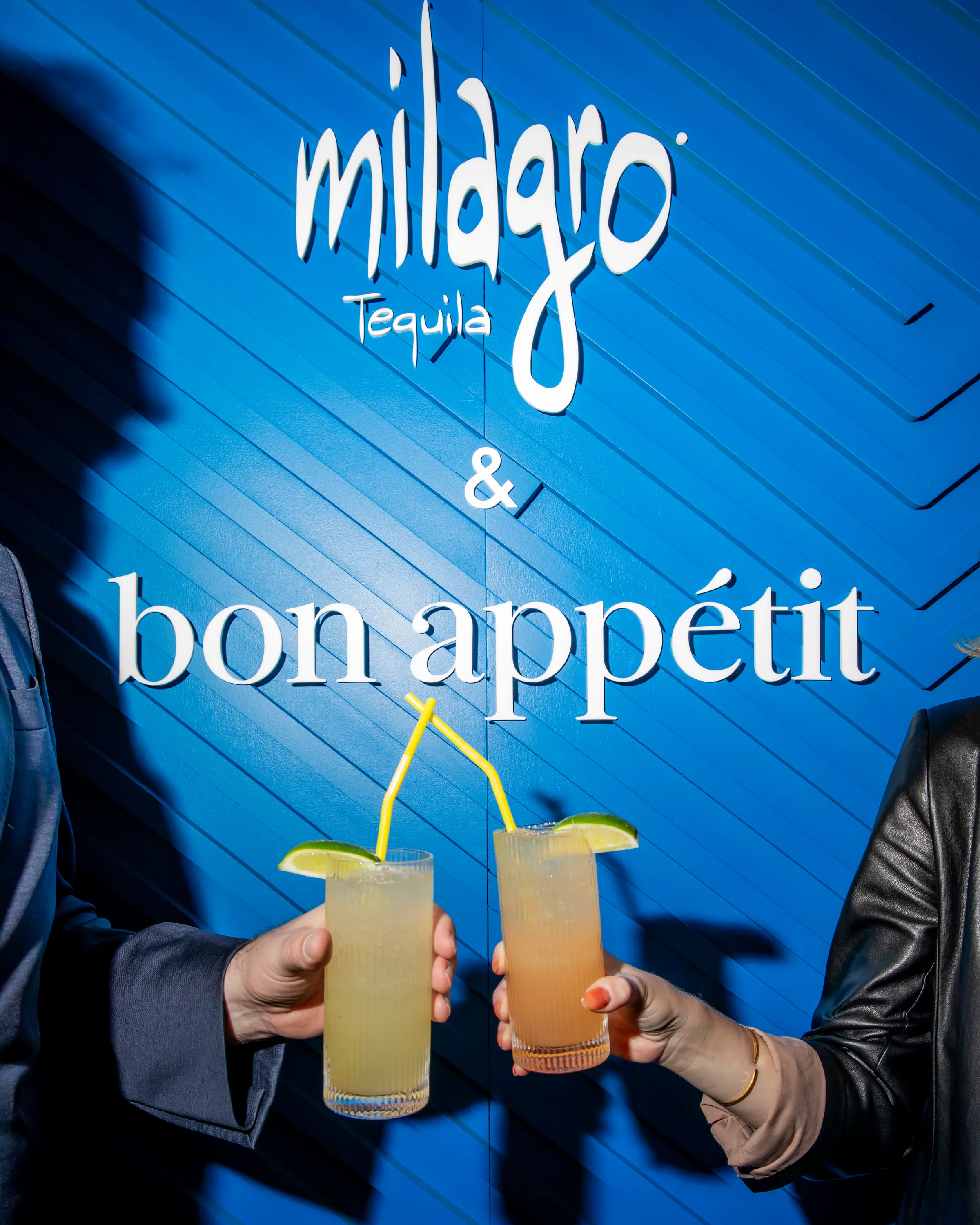 Two cocktails raised in front of the backdrop